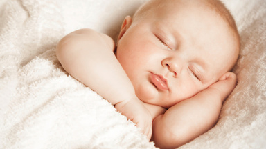 Ein Neugeborenes schläft friedlich in einer weißen Decke