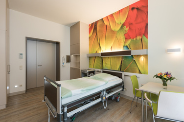 Helles Patientenzimmer mit Pflegebett und großem Wandbild auf der Palliativstation